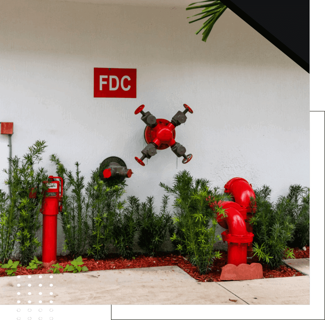 A red drone flying indoors near fire safety equipment and greenery.